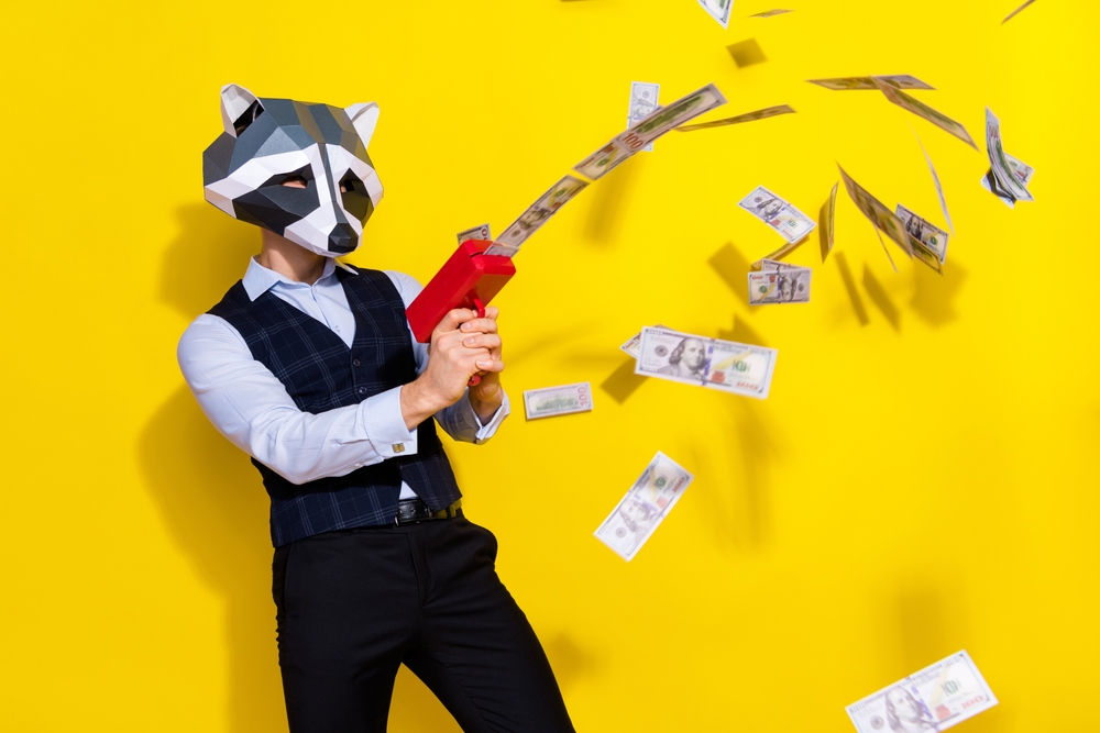 Man with Raccoon Mask happily shooting money from gun